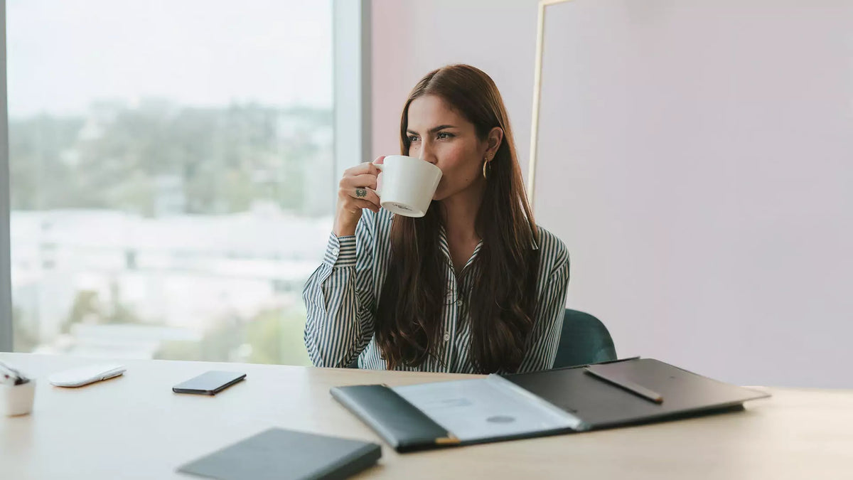 Führungskraft im gestreiften Hemd am Schreibtisch mit Kaffee, vor ihr eine geöffnete Mappe mit ihrem Lebenslauf