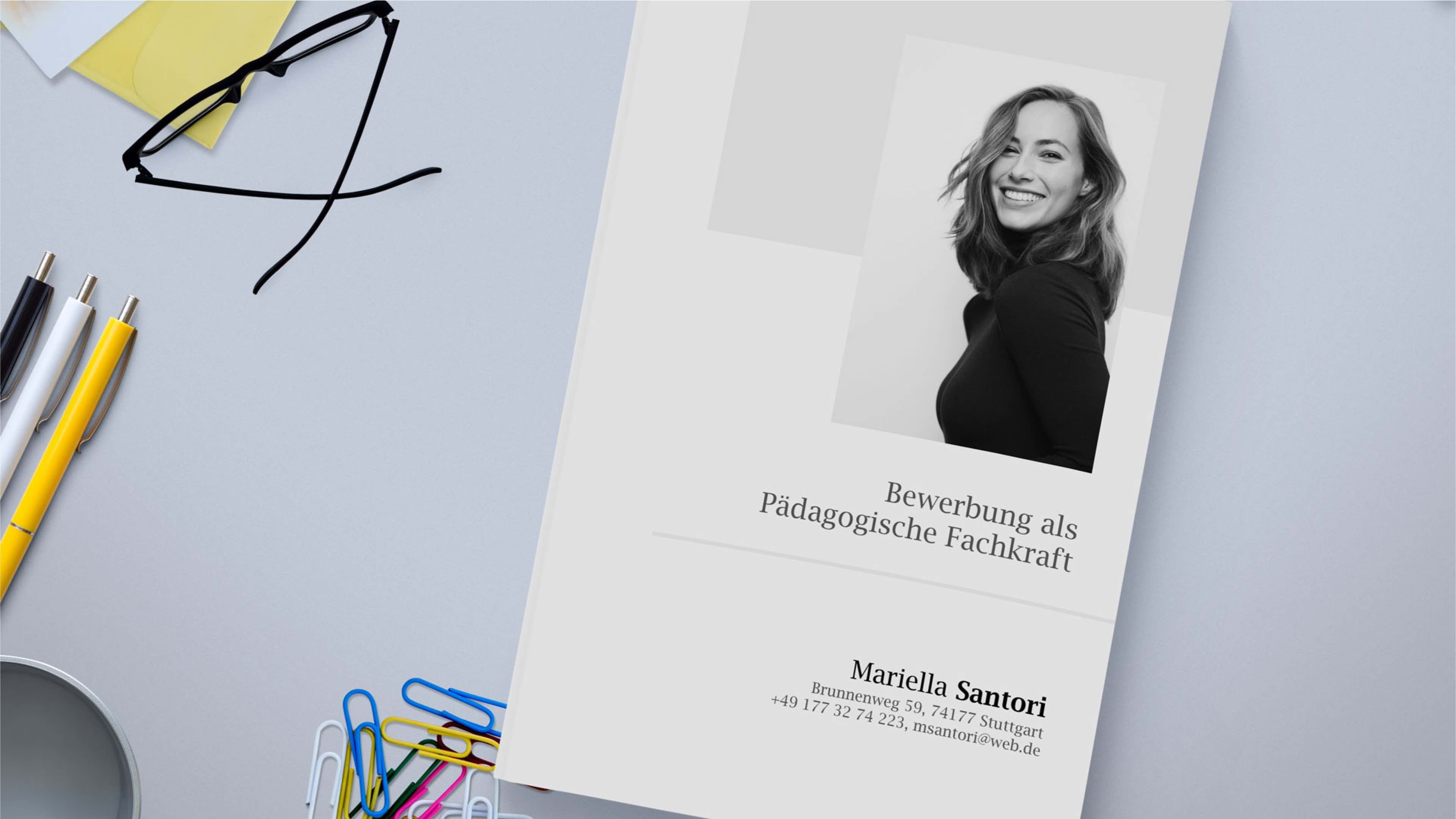 Ein Anschreiben mit einem Schwarzweißfoto einer lächelnden Frau auf der rechten Seite. Der Text lautet „Bewerbung als pädagogische Fachkraft“ und die Kontaktdaten von „Mariella Santori“. Daneben liegen eine Brille, Buntstifte, eine Tasse und Büroklammern.